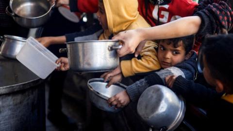 Palestinian children holding empty pots and boxes waiting for food