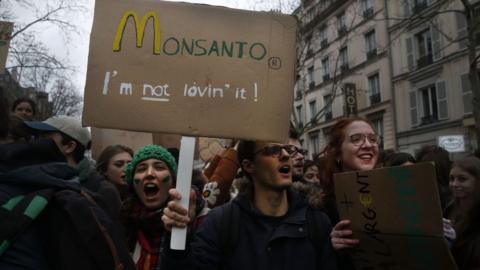 A Youth protester holds a banner reading "Monsanto, I'm not loving it" during a demonstration
