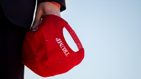 Former US President Donald Trump holds his cap during arrival at a rally at the Waco Regional Airport on 25 March 2023 in Waco, Texas