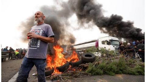 A man stands near a fire as farmers block a highway in Spain