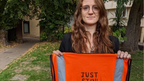 Stephanie Aylett outside Chelmsford Magistrates Court holding up a high viz with Just stop oil written on the back