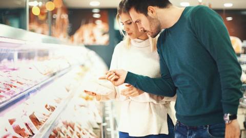 Stock image of two people looking at meat in a supermarket