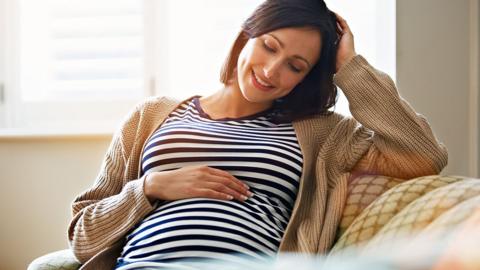 Pregnant woman holding stomach wearing striped t shirt.