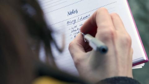 Close up of a hand writing in a notebook with the heading 'blog ideas'.