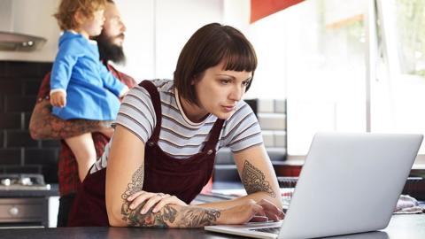 Woman looking at laptop in kitchen with man and baby in background