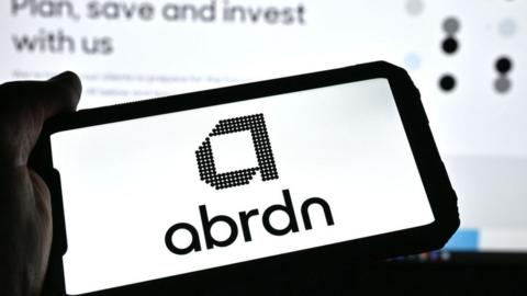 Person holding a phone with the Abrdn logo on it