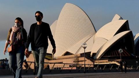 People wearing masks walk past the Sydney Opera House during a state-wide lockdown in August 2021