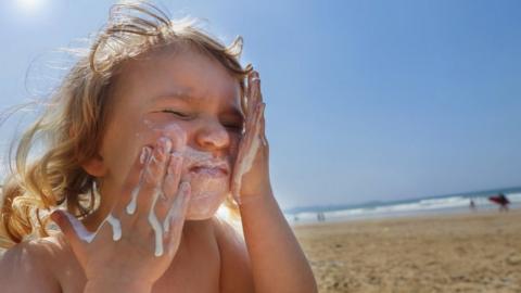 A child putting sun cream on their face at the beach