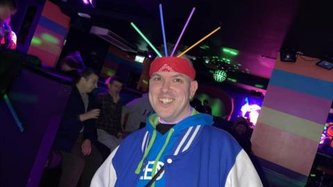 A man smiling for a picture with glowsticks on his head