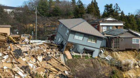 Damaged houses, including one totally collapsed (C), are pictured along a street in Wajima, Ishikawa prefecture on January 2, 2024