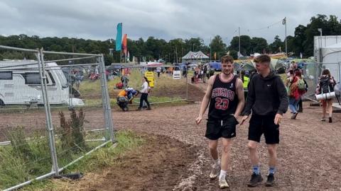 Festival-goers on a muddy walkway at the site