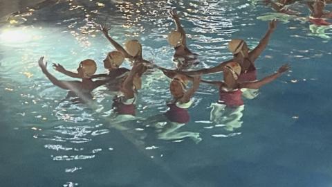A group of synchronised swimmers with their arms in the air