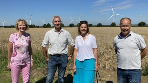 Two men and two women line up in a field in front of wind turbines
