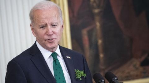 Joe Biden, sporting a shamrock tie and sprig of shamrock in his jacket pocket, speaks at a lectern
