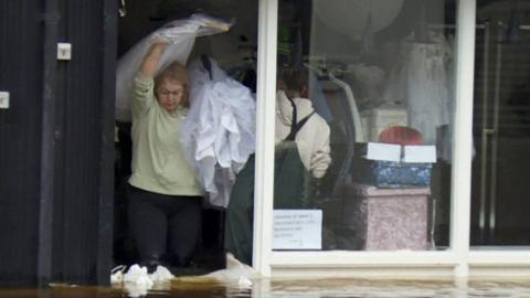 woman carrying wedding dresses out of flooded shop