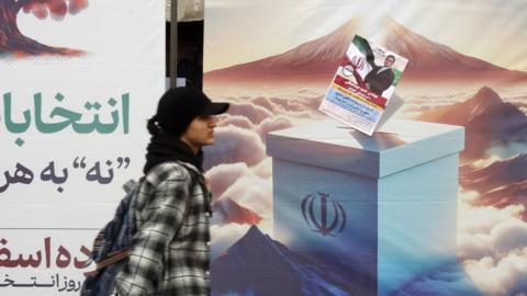An Iranian woman walks past some general election billboards in Tehran
