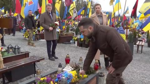 President Zelensky laying flowers, surrounded by Ukrainian flags