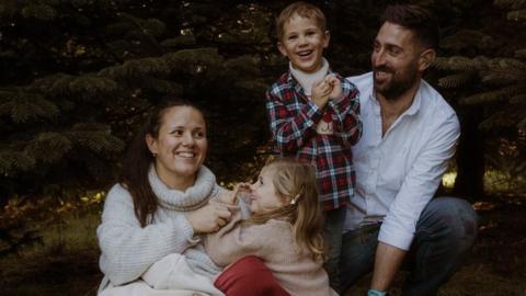 Karen and James Marks sitting on the ground with their three young children, all smiling