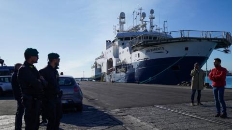 Police officers stand near the gate next to rescue ship Geo Barents, run by Doctors Without Borders (MSF), in the port of Catania