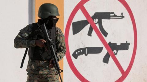 A soldier stands guard next to a sign prohibiting the use of weapons outside the military headquarters as Haiti continues in a state of emergency, in Port-au-Prince, Haiti March 6, 2024. R