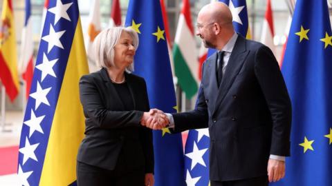 Chairwoman of the Council of Ministers of Bosnia and Herzegovina Borjana Krišto shaking hands with European Council president Charles Michel standing in front of flags