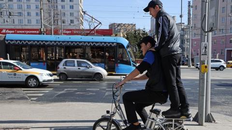 Two work migrants from Kyrgyzstan ride bicycle on the street, April,14,2023, in Moscow, Russia.
