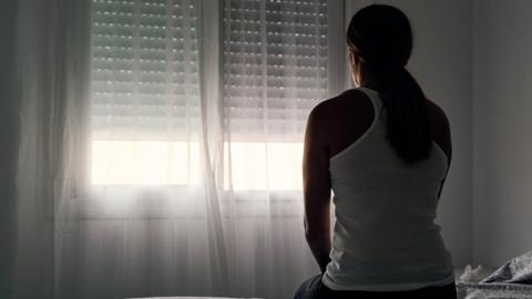 Anonymous woman sitting on a bed looking out the window