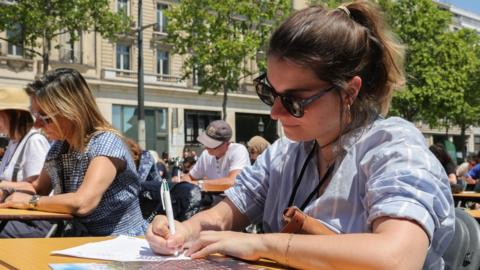 A participant writes on a sheet of paper during 'The World's Biggest Dictation' on the Champs Elysees in Paris, France, 04 June 2023. The Champs-Elysees Committee, organizers of the event, expect around 1,700 participants to take part in the challenge, an attempt to validate the Guinness Book World Record for the world's largest spelling test.