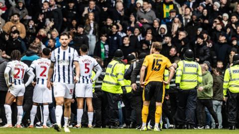 Players of West Bromwich Albion and Wolverhampton Wanderers watch on as stewards and local police officers attempt to quell clashes between rival fans during the FA Cup fourth-round tie