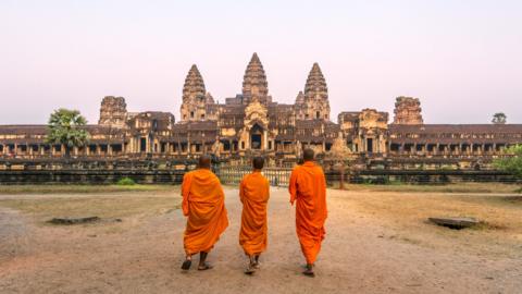 Three people walk towards the Angkor Wat temple