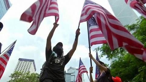 A man waves two US flags - one in each hand - in this frame