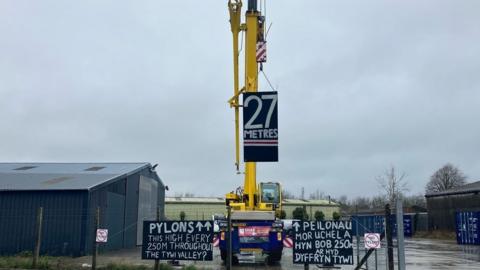 a crane in a car park with signs saying 27 metres and this is how high the pylons will be