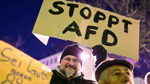 A man holds up a placard reading "Stop AFD" during a demonstration against right extremism and the policy of Germany's far-right the Alternative for Germany (AfD) party, on January 16, 2024 in Cologne