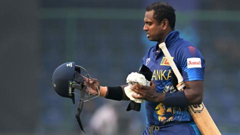 Sri Lanka's Angelo Mathews looks at his broken helmet after being timed out in the World Cup match against Bangladesh