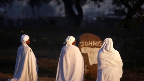 Three women in white kneeling down praying in Harare