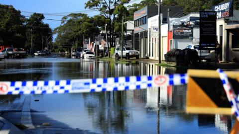 Police tape is pictured in front of a closed-off flooded road in the Sydney suburb of North Narrabeen on 6 April