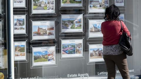 People looking at houses for sale in an estate agents window in Cirencester, Gloucestershire