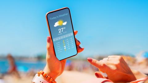 A woman looks at the weather forecast on her phone on the beach