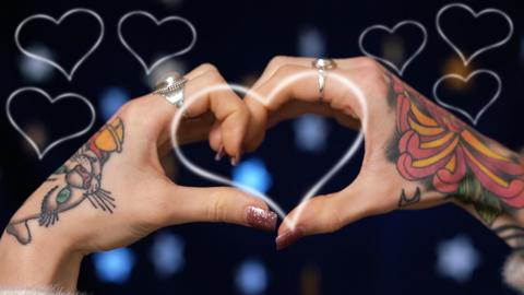 A pair of hands forming a heart with colourful tattoos and heart outline graphics.