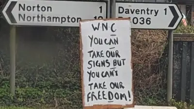 Handpainted sign attached to road sign saying "WNC You can take our signs but you can't take our freedom"