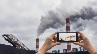 Hand holding black smartphone while photographing a coal-fired power plant