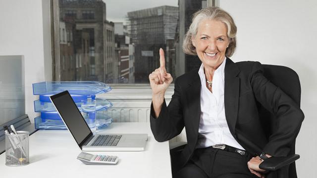 Улыбающаяся пожилая женщина за офисным столом