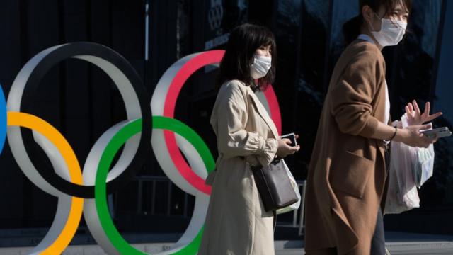 Люди в масках на фоне олимпийских колец