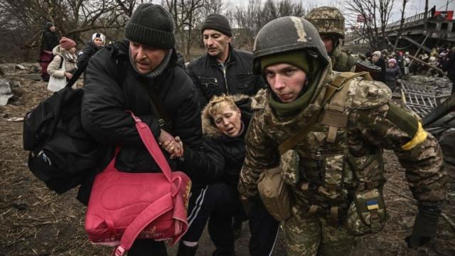 Явно виснаженій жінці надають допомогу під час переходу через зруйнований міст у місті Ірпінь на північний захід від Києва