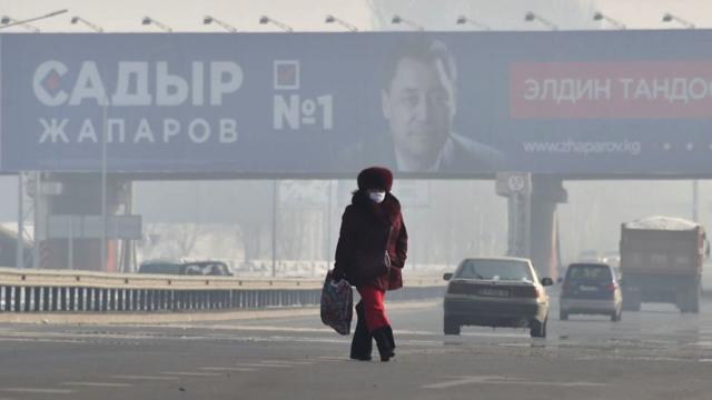 Женщина на фоне предвыборного плаката Жапарова в густом смоге