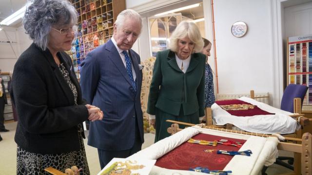 King Charles III and the Queen Consort look at their throne seat covers during a visit to the Royal College of Needlework at Hampton Court Palace