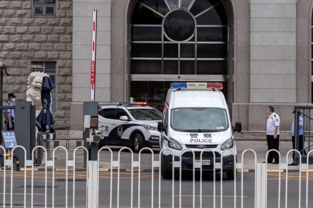 Две полицейские машины выезжают из ворот здания суда