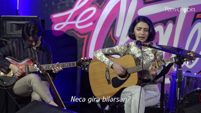 Две девушки сидят на сцене с гитарами. Одна поет.