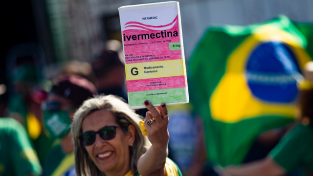 Участница демонстрации в поддержку президента Бразилии Болсонару, известного скептическим отношением к коронавирусу, держит плакат в виде упаковки ивермектина