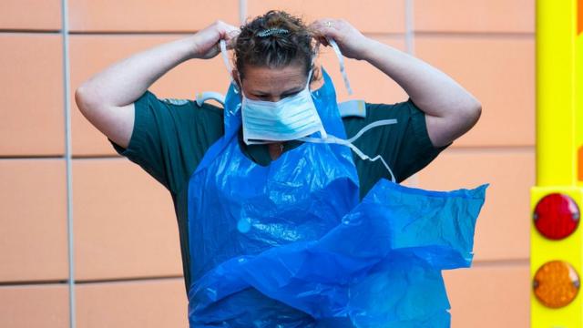 Работник скорой помощи в Британии надевает защитную маску